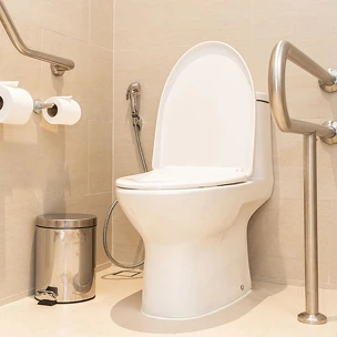 Des toilettes blanches aménagées dans une salle de bains, à côté d'une poubelle.